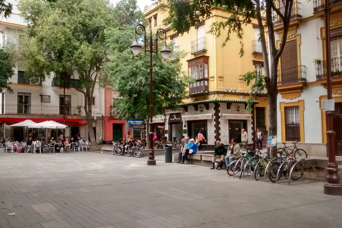 Plaza de la Alfalfa in Seville: a paved square with café tables under trees, bicycles in racks and yellow and white buildings with balconies